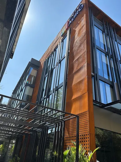 A low-angle shot of the Sattva Auro commercial building, emphasizing the verticality of the glass and steel elements against the corten steel cladding.