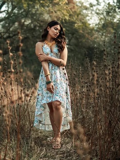 This portrait uses the natural frame of the trees and tall grass to create a sense of depth. The model's pose is soft and contemplative, contributing to the overall calm and organic mood of the outdoor shoot.