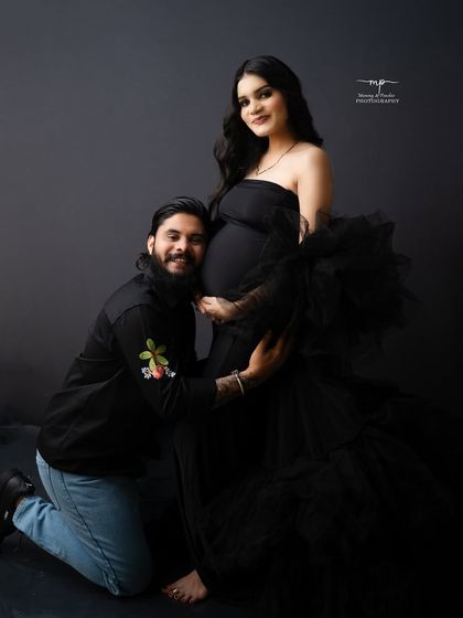 A powerful and stylish maternity portrait against a dark backdrop. The husband-to-be embraces his wife from his knees, creating a pose of adoration and strength.
