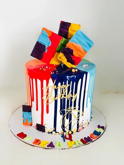 A vibrant and artistic cake with colorful drips and abstract chocolate shards. This design is a celebration of color and flavor, perfect for a modern birthday party.