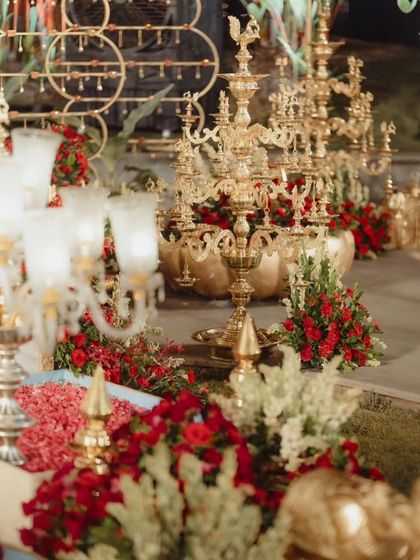 An artful arrangement of traditional brass lamps and floral decorations. The gleaming gold of the brassware contrasts beautifully with the deep red of the roses and the fresh white of the tuberoses.