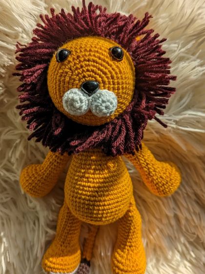 A proud lion amigurumi with a full, dark red mane and a golden-yellow body.
