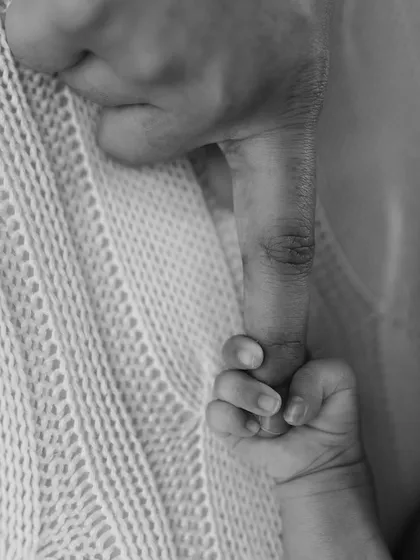 A macro shot of a baby's hand gripping a parent's finger, rendered in beautiful black and white.
