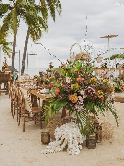 A long dining table set for a sunset meal on the beach in Mauritius, surrounded by exotic flowers and palm trees.