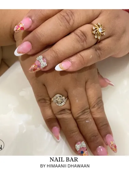 A close-up of a glamorous set with glitter, French tips, and 3D bow charms made of sparkling rhinestones.