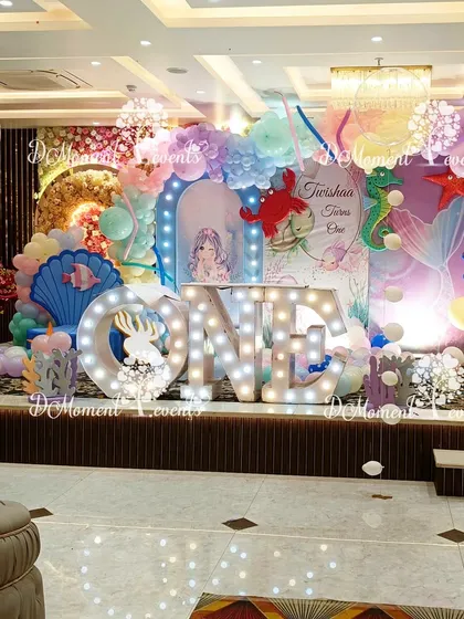 A magical mermaid-themed first birthday stage. This setup features a large "ONE" marquee sign, pastel balloon arrangements, and various under-the-sea elements like shells and seahorses, creating a dreamy underwater scene.