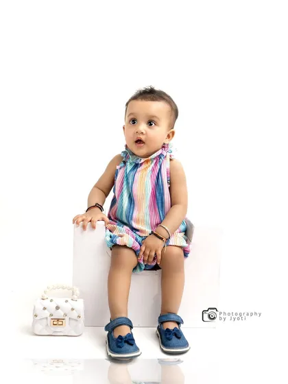 A chic and stylish studio portrait against a pure white background. The baby's colorful striped outfit and the simple white block create a modern, high-fashion look.