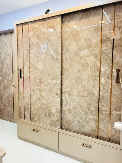 A sliding wardrobe with a luxurious marble-finish laminate and gold accents. This design includes drawers at the bottom for easy access to smaller items.