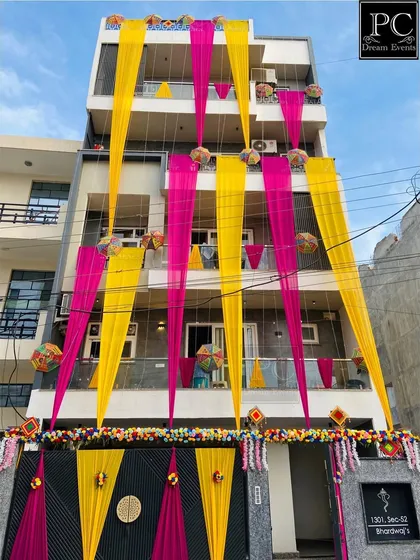 A full view of a house decorated for a wedding. The combination of bright pink and yellow drapes, along with traditional hangings, announces the celebration to the whole neighborhood.