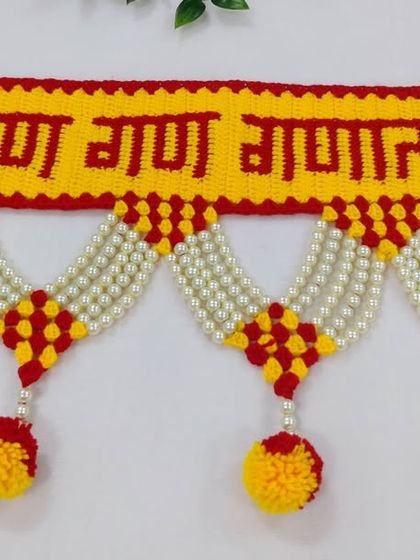 A close up of the "गण गण गणात बोते" toran, showing the clear lettering and the neat crochet work, complemented by pearl strings and pom-poms.