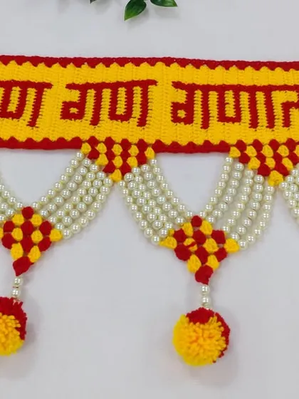 A close up of the "गण गण गणात बोते" toran, showing the clear lettering and the neat crochet work, complemented by pearl strings and pom-poms.