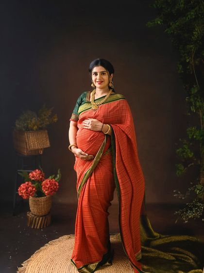 A full length portrait of the mom to be in a beautiful red and green cotton saree. Her confident stance and gentle smile radiate the joy of motherhood.