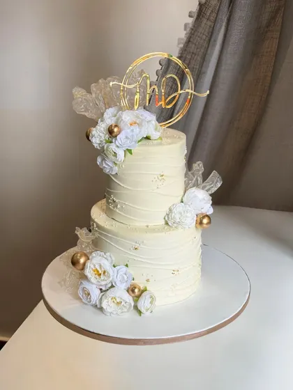 A bride envisioned a minimalist design with a touch of elegance, and this two-tier beauty was the result. Crafted in classic white with delicate gold accents and a custom initial topper, it’s simply timeless.