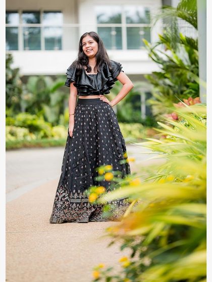 A full-length portrait of a young woman in a stylish black crop top and skirt, posing confidently during a family photoshoot.