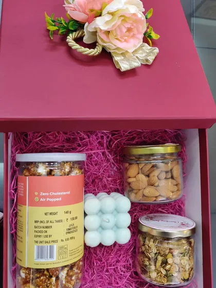 A premium red gift box filled with jars of popcorn, almonds, and muesli, along with a trendy bubble candle.