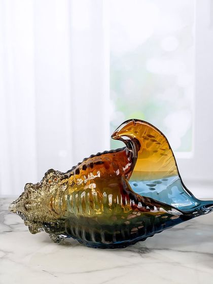 This stunning handblown glass conch shell captures the colors of a sunset over the ocean. The blend of amber, brown, and blue makes it a beautiful and serene coastal-inspired showpiece.