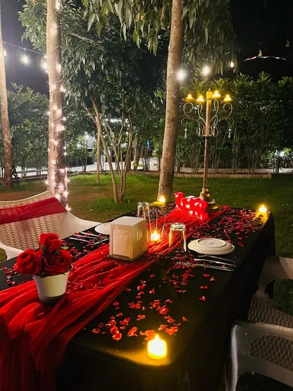 I arrange intimate, romantic dinners for two in any outdoor setting. This garden setup includes a fully set table with a red runner, rose petals, a classic candelabra, and ambient lighting from surrounding LED candles and overhead string lights.