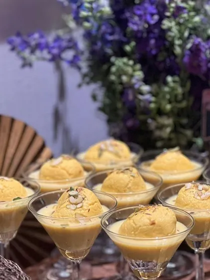 A modern presentation of Rasmalai, served in elegant martini glasses. The creamy, saffron-infused milk and soft cheese dumplings are garnished with nuts.