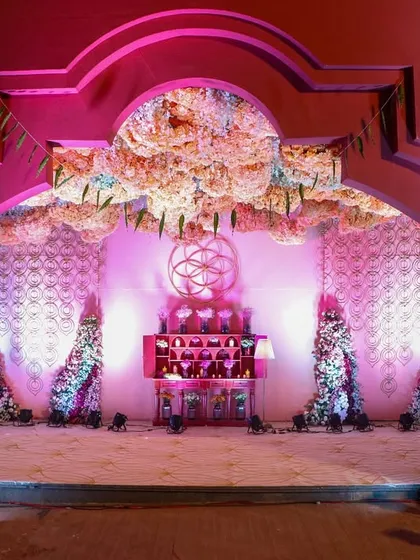 A grand archway frames the view into the 'Anant' themed event space, with a stunning floral cloud overhead and intricate decor drawing guests into the celebration.