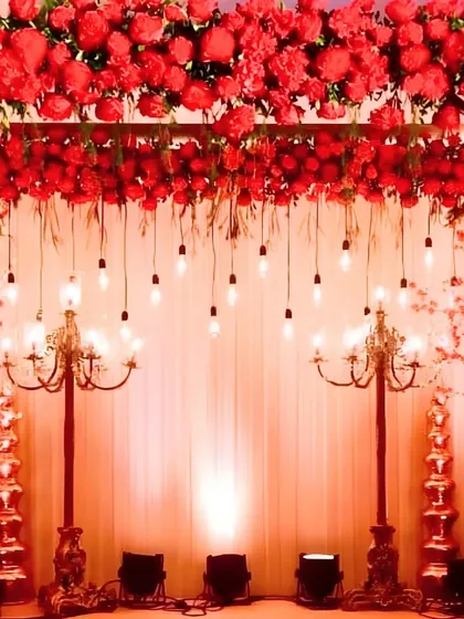 A dramatic and romantic stage bathed in red light, featuring a canopy of red flowers, hanging Edison bulbs, and ornate candelabras for a vintage glam look.