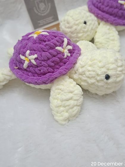 A pair of white plush turtles with purple, flower-adorned shells.