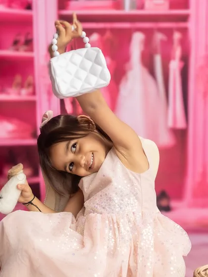 A big sister is so excited about her new role, posing with her baby sister in a fun, pink-themed photoshoot.