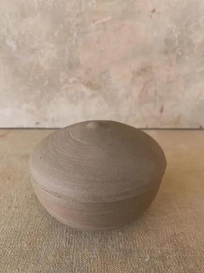 A raw, unglazed lidded jar, closed. Its simplicity is its strength.
