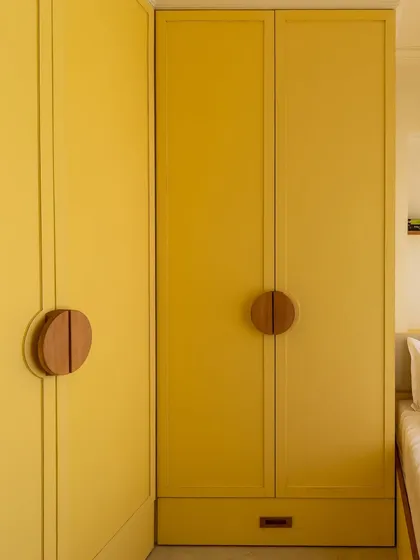 A close-up of the custom circular wooden handles on the yellow wardrobe, an example of our focus on small details that make a big impact.