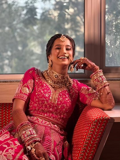 Relaxing by the window, the bride looks effortlessly chic and happy. Her natural smile and radiant makeup make for a perfect, joyful bridal portrait.