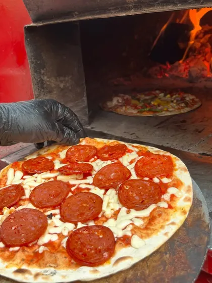A chef carefully places a pepperoni pizza into the intense heat of our wood-fired oven. This is the final step to achieving that perfectly charred, bubbly crust.