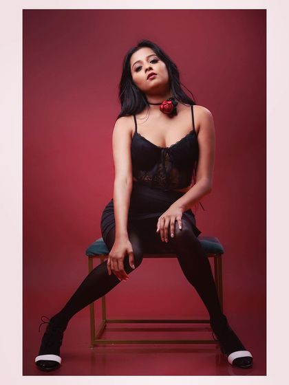 A full-length shot of a model in a glamorous black outfit against a red background. The pose is strong and confident, creating a striking fashion image.