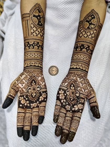 This bridal henna for Nadia features a beautiful mix of styles. The palms have a floral and paisley design, while the arms showcase bold, dark bands with intricate details inside.