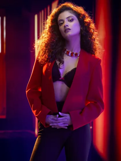 A powerful and dramatic shot using colored lighting. The mix of red and blue light creates a moody, futuristic atmosphere that highlights the model's strong pose and the bold red jacket.