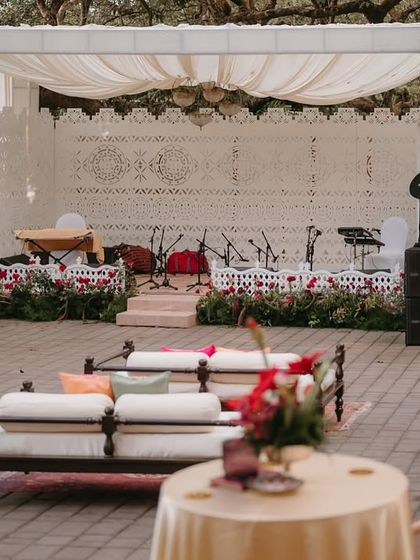 A focused shot of the Qawali night stage, highlighting the intricate white backdrop, soft fabric draping, and a line of red flowers that adds a pop of color.