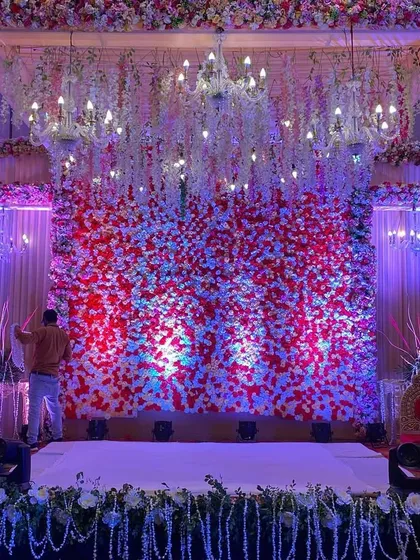 An indoor mandap or small stage with a stunning backdrop of red and white flowers and hanging crystal chandeliers.