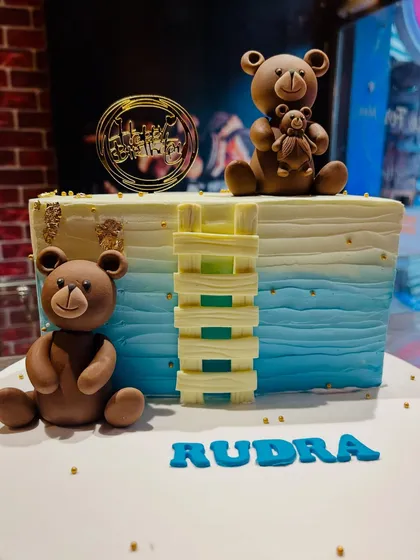 A rectangular teddy bear cake with a blue ombre effect, featuring two fondant bears and a Jenga-like block structure.