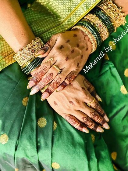 This photo shows an elegant and simple engagement mehendi design on the back of the hands, paired with traditional green bangles. The focus is on the rich, dark stain.