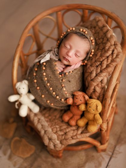 Wrapped in love with his teddy bear friends. The earthy tones of the wrap, bonnet, and chunky knit blanket create a warm and comforting scene.