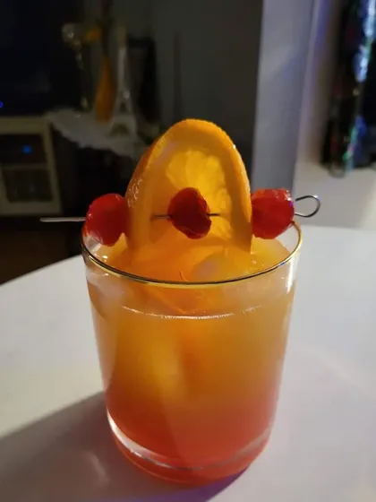 A classic Tequila Sunrise mocktail. The beautiful gradient of orange and red makes it a visually stunning drink, garnished simply with an orange slice and cherries.