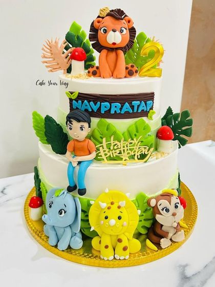 A two-tier jungle cake with a personalized touch, featuring a fondant figure of the birthday boy among his favorite animals.