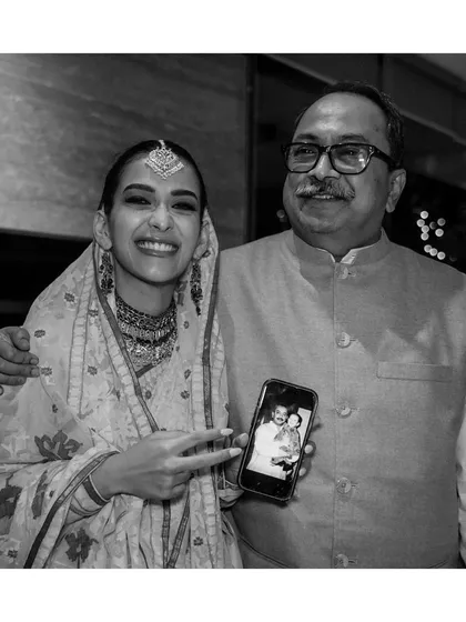 A bride poses with her father, who holds up a childhood photo of them on his phone. This then-and-now moment is a beautiful, emotional tribute to their bond and the journey to this day.