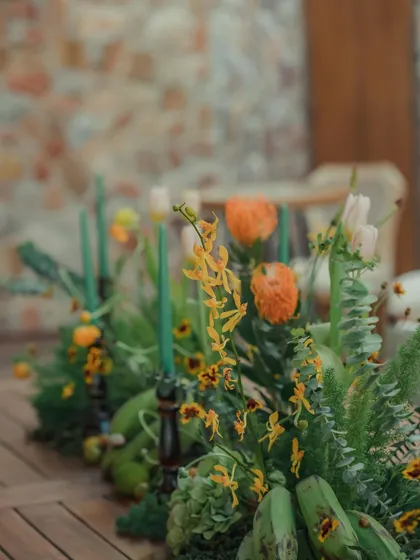 Another detail of the autumnal tablescape, showing a mix of yellow and orange flowers with green foliage. The arrangement feels wild, organic, and perfectly suited to the natural surroundings.