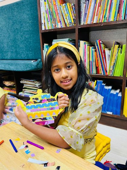 A proud young artist shows off her colorful teapot craft. During the party, each child gets to decorate their own paper teapot, a wonderful keepsake to take home.
