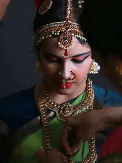 A behind-the-scenes candid from the Arangetram shoot, showing the dancer getting help with her intricate jewelry. These "getting ready" moments are filled with quiet emotion and anticipation.
