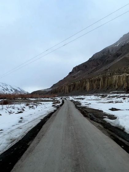 An empty road stretching through a snow-lined valley in Spiti.