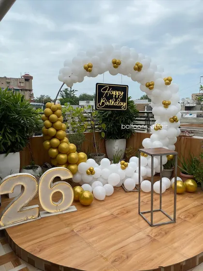 An elegant and modern 26th birthday setup on a rooftop terrace. This decoration features a stylish white and gold balloon semi-arch, large marquee light-up numbers, and a custom 'Happy Birthday' sign, perfect for a chic outdoor celebration.