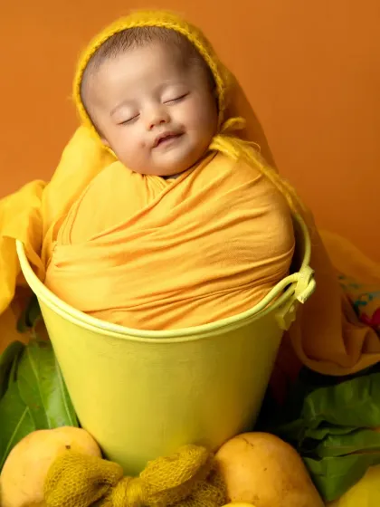 A peaceful newborn sleeps soundly in a yellow bucket, part of our sweet summer mango-themed session.