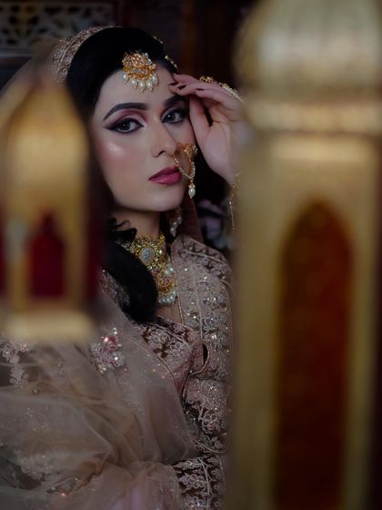 A creative shot through a prop, focusing on the bride's expressive eyes and flawless makeup.