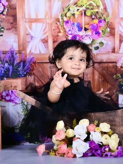 A baby girl in a black dress surrounded by a beautiful floral arrangement.