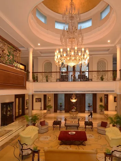 A grand, double height foyer showcasing neo classical design. The symmetrical layout, massive chandelier, and detailed ironwork on the balustrade speak to a timeless and opulent aesthetic.